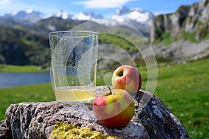 Glass of natural Asturian cider made fromÂ fermented apples with view on Covadonga lake and tops of Picos de Europa mountains,